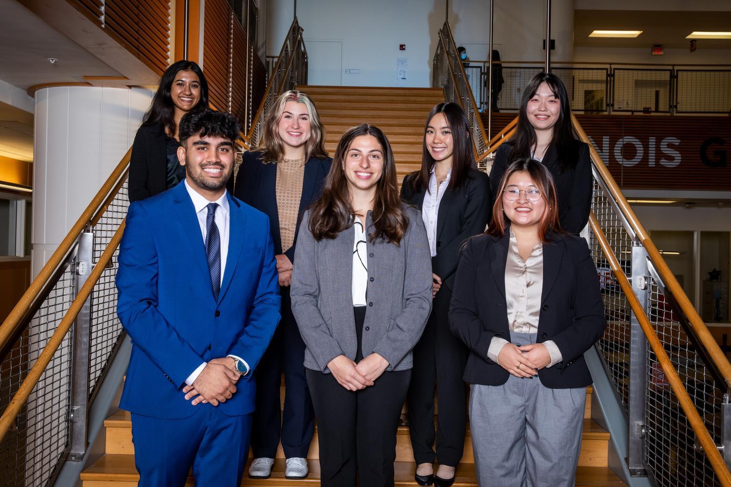 Students standing with arms crossed in suits facing camera.